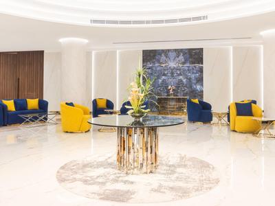 Světlá hotelová lobby s moderními žluto-modrými křesly a centrálním stolem s květinovou dekorací.