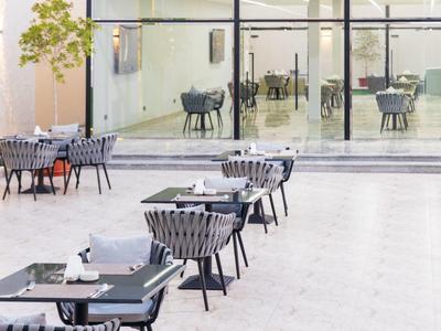 Moderní venkovní prostor hotelu se šedými židlemi a černými stoly na světlé dlážděné terase.