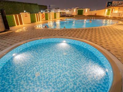 Osvětlený venkovní bazén a vířivka s mozaikovými dlaždicemi v hotelu v noci.