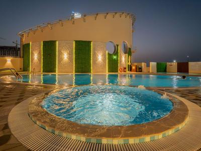 Osvětlený bazén a vířivka na střeše v noci s výhledem na město.