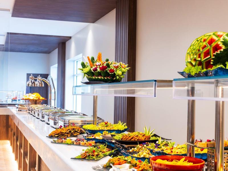 Dlouhý bufetový stůl s různými pokrmy a zdobenými melouny v jídelně.