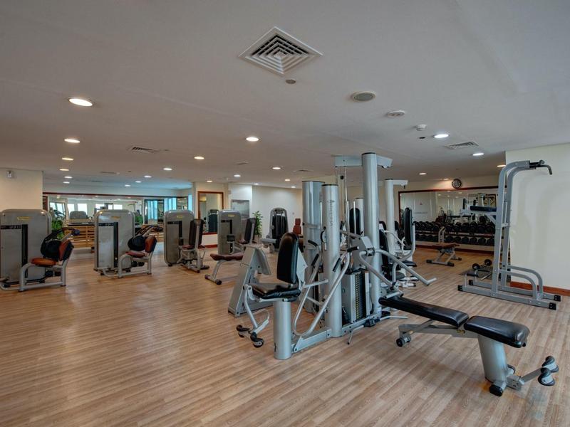 Moderní fitness s různými tréninkovými stroji a dřevěnou podlahou.