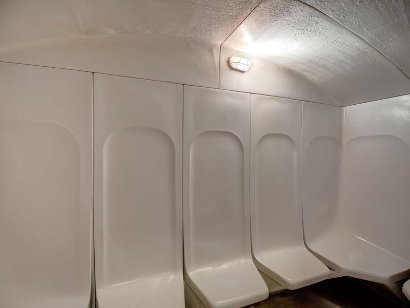 Bílé plastové sedadla před bílou stěnou v místnosti s klenutým stropem a světlem.