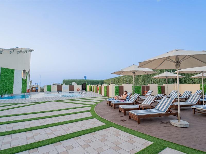 Venkovní prostor moderního hotelu s lehátky, slunečníky a čistou oblohou.