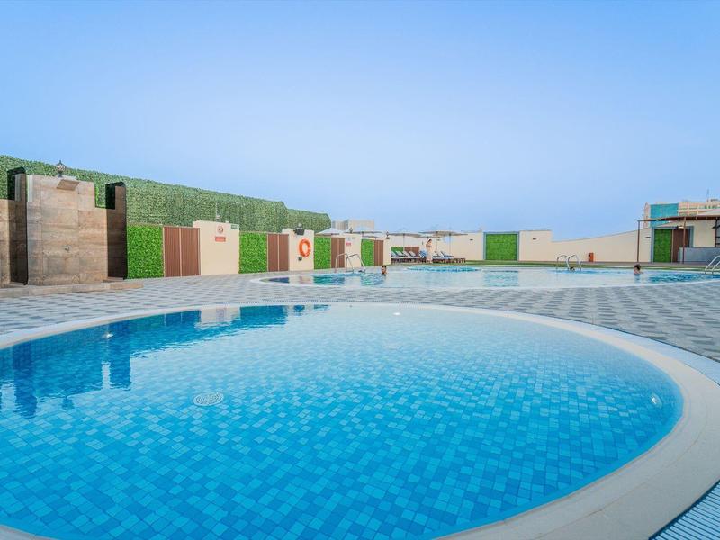 Kruhový venkovní bazén s čistou modrou vodou a posezením pod slunečnou oblohou.