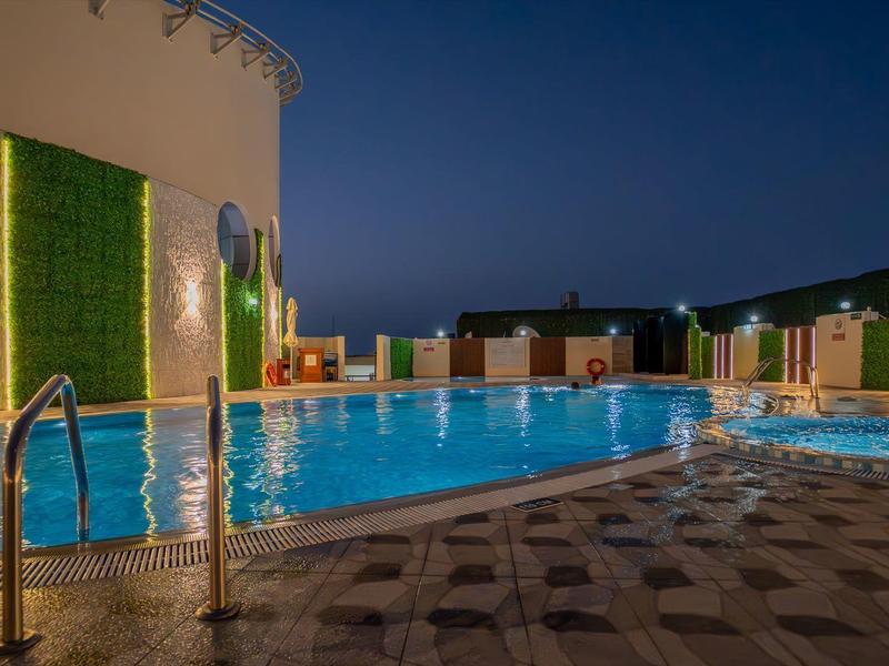 Osvětlený venkovní bazén v hotelu v noci s posezením kolem bazénu.