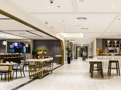 Espacioso y moderno salón de hotel con mesas, sillas y un bar a la derecha.