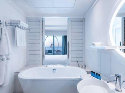 Baño moderno blanco con bañera independiente y gran espejo en la habitación del hotel.