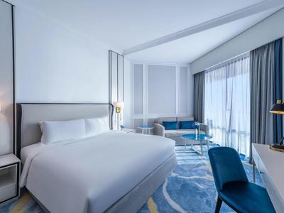 Habitación de hotel moderna con cama grande, silla, escritorio y balcón con vistas exteriores.