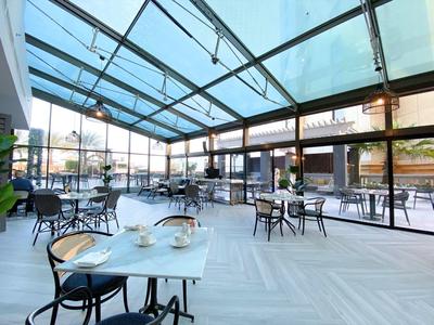 Amplio y luminoso invernadero con techo de vidrio y mesas cuadradas, ideal para hoteles y cafeterías.