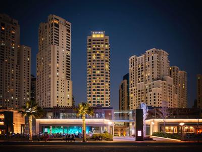 Vista nocturna de la ciudad con rascacielos iluminados y un bar de hotel moderno en primer plano.