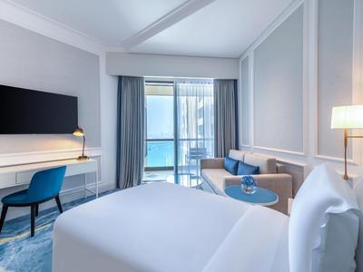 Habitación de hotel moderna con cama grande, escritorio, silla y balcón con vista a la piscina.