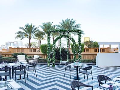 Moderna terraza de hotel con suelo en zigzag blanco y negro, palmeras y áreas de descanso elegantes.