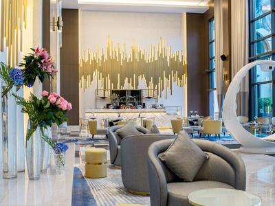 Lobby de hotel moderna con sillones elegantes, decoración floral y luz natural de grandes ventanas.