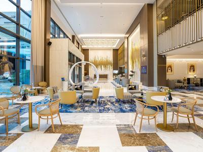 Área de vestíbulo de hotel moderna y luminosa con alfombras azules y muebles claros de diseño elegante.