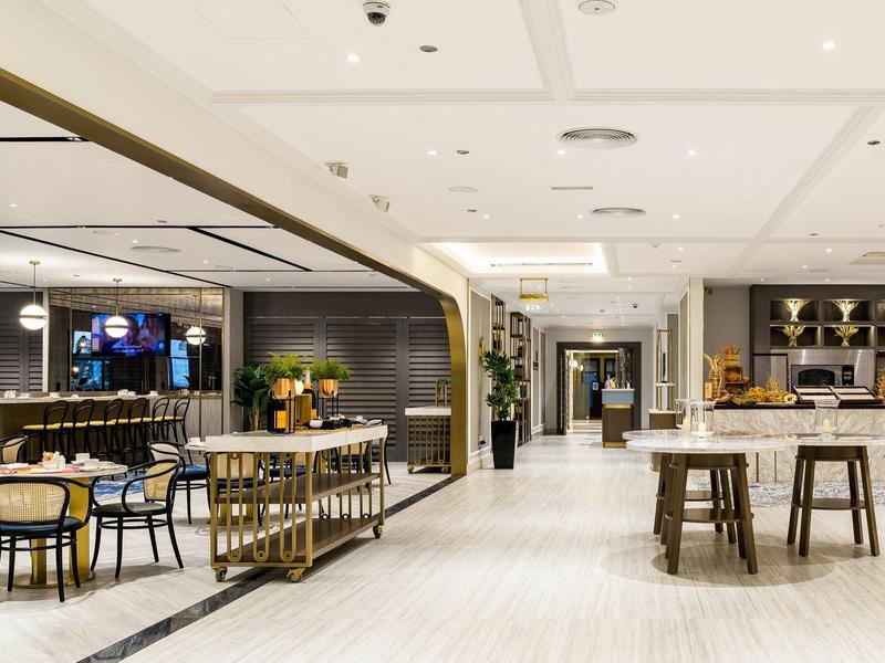 Espacioso y moderno salón de hotel con mesas, sillas y un bar a la derecha.