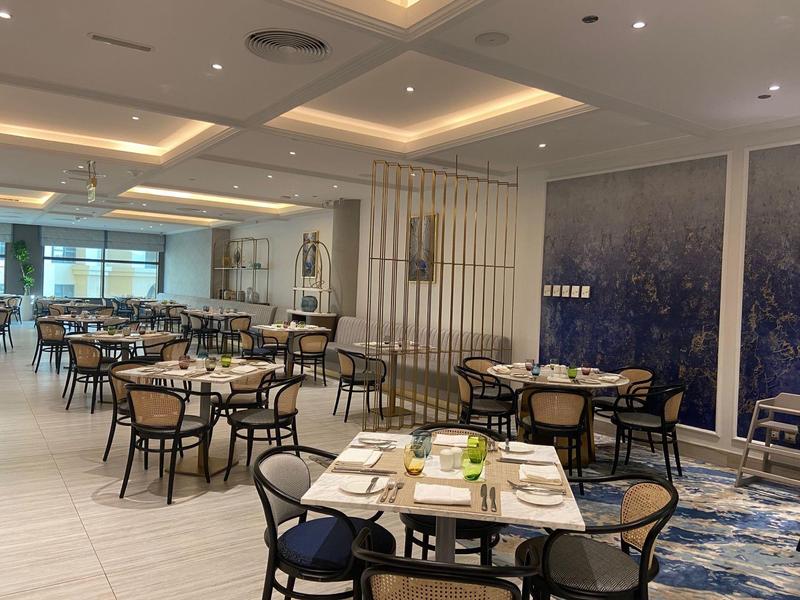 Comedor moderno de hotel con mesas puestas, sillas y iluminación elegante.