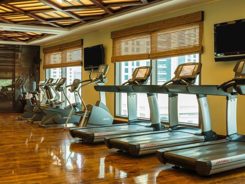 Gimnasio luminoso con cintas de correr frente a grandes ventanas y suelo de madera en el hotel.