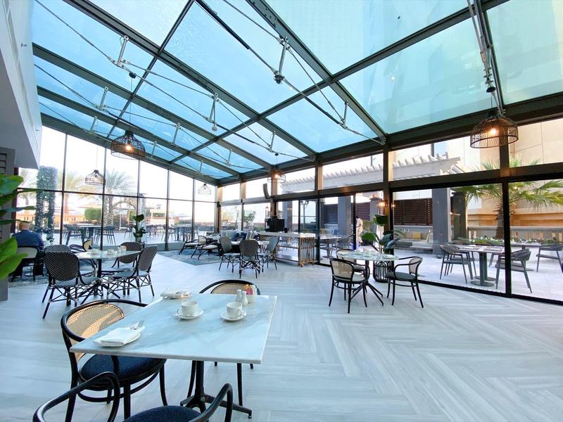 Amplio y luminoso invernadero con techo de vidrio y mesas cuadradas, ideal para hoteles y cafeterías.