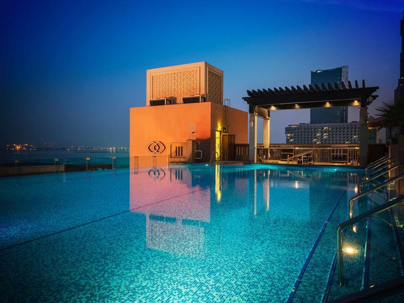 Área de piscina iluminada en la azotea con vista a la ciudad al anochecer.