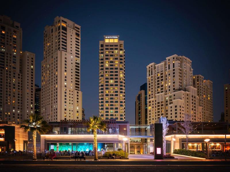 Vista nocturna de la ciudad con rascacielos iluminados y un bar de hotel moderno en primer plano.