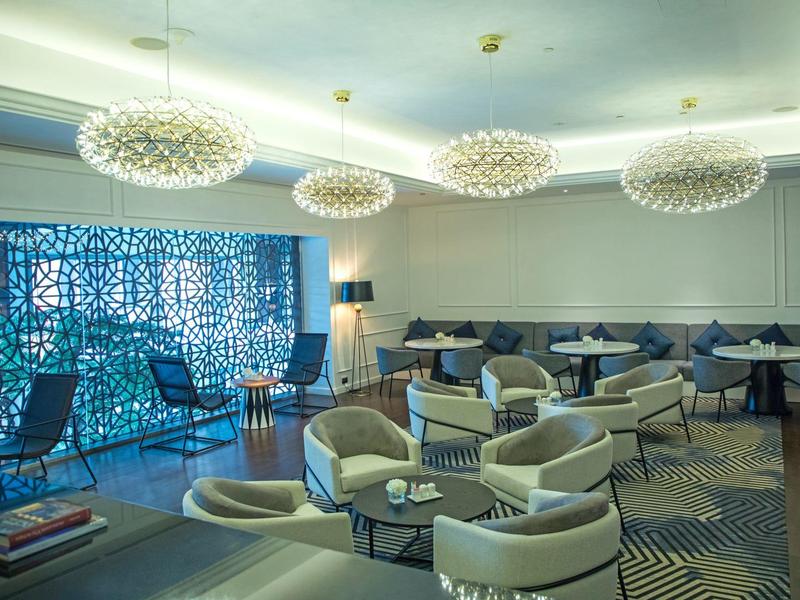 Área lounge moderna de hotel con sillones elegantes, mesas y candelabros decorativos en el techo.