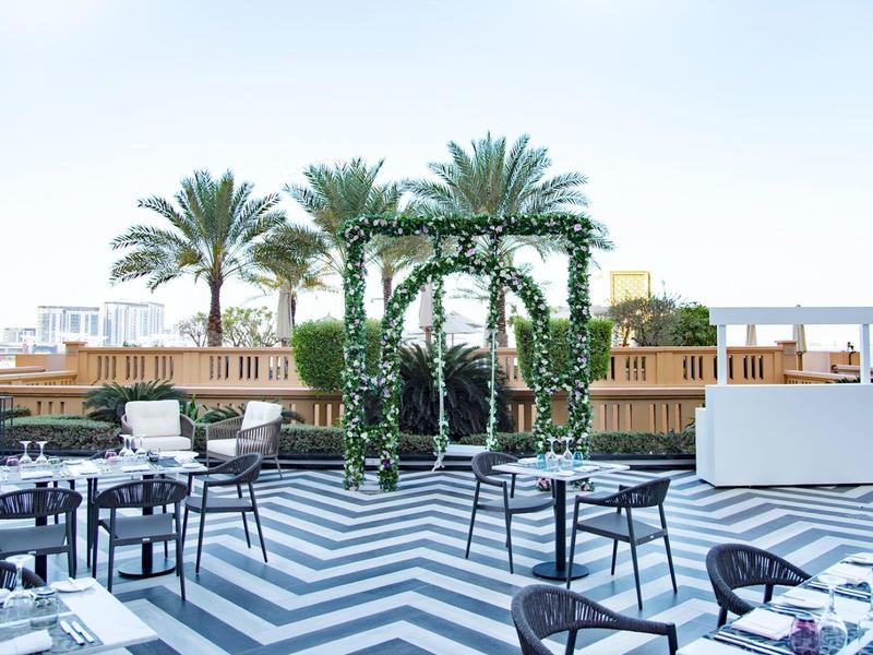 Moderna terraza de hotel con suelo en zigzag blanco y negro, palmeras y áreas de descanso elegantes.