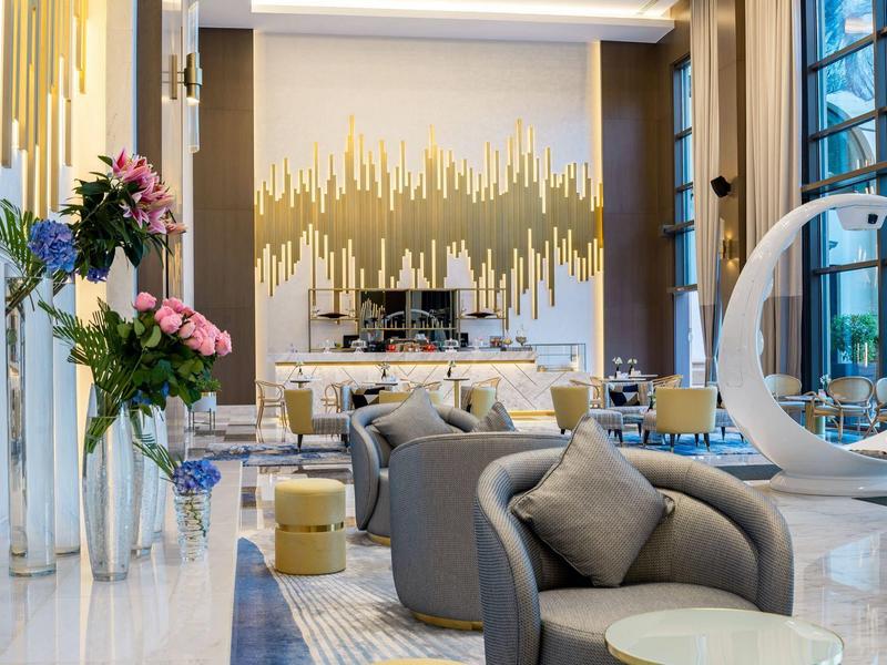 Lobby de hotel moderna con sillones elegantes, decoración floral y luz natural de grandes ventanas.