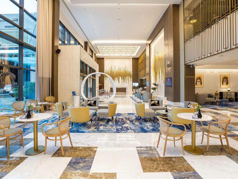 Área de vestíbulo de hotel moderna y luminosa con alfombras azules y muebles claros de diseño elegante.
