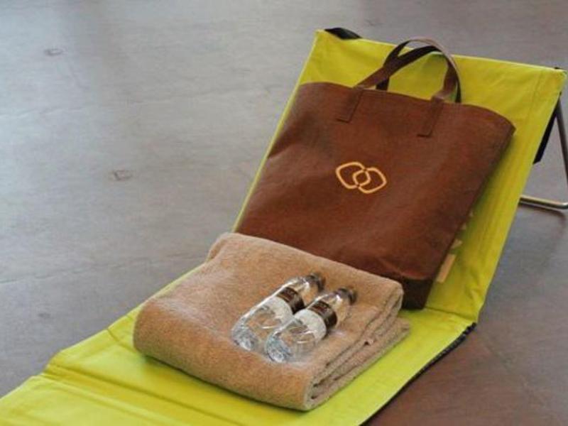 Tumbona amarilla con bolsa marrón y toalla con botellas de agua encima.