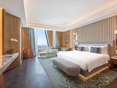 Bright hotel room with large bed, sofa, rug, and window with an outside view.