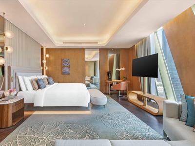 Modern hotel room with large bed, TV, cozy seating area, and large windows.