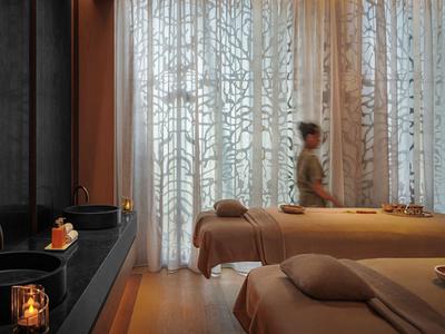 Relaxation area with two beige massage tables, decorative curtain, and soft lighting.