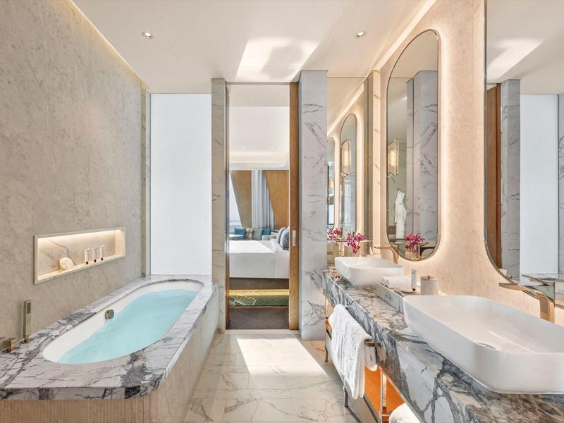 Modern bathroom with large bathtub and illuminated mirrors in light marble.
