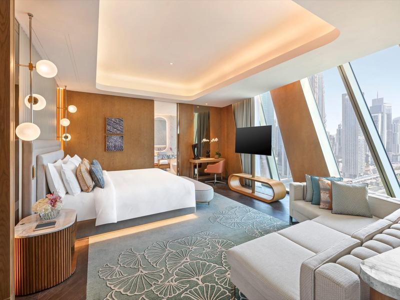Modern hotel room with large bed, sofa, panoramic windows, and city view.