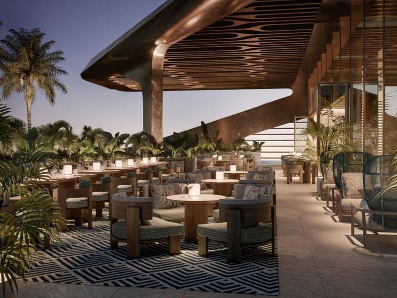 Evening hotel terrace with tables, chairs, and palm trees under a covered roof.
