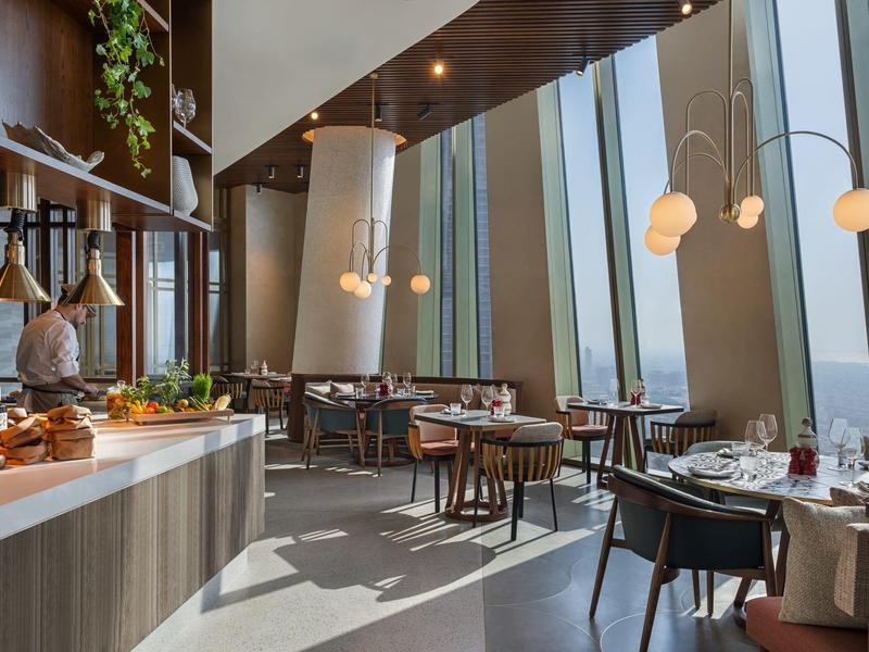 Modern restaurant with floor-to-ceiling windows, elegantly set tables, and warm wood design