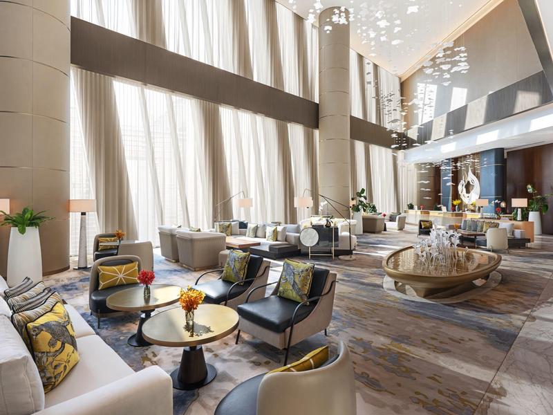 Elegant hotel lounge with tall windows, modern furniture, and neutral tones.
