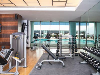 Moderner Fitnessraum mit Hanteln, Kraftgeräten und großen Fenstern mit Aussicht.