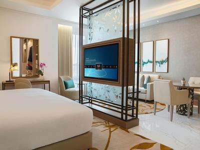 A modern hotel room with a large bed, seating area, and a decorative room divider with TV.