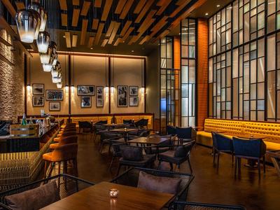 Modern eingerichtete Hotelbar mit holzverkleideter Decke, Sesseln und großen Fenstern.