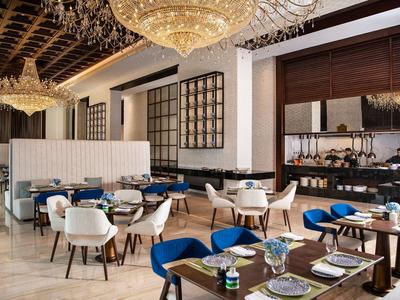 Elegant hotel restaurant with blue and white chairs, set tables, and chandeliers.