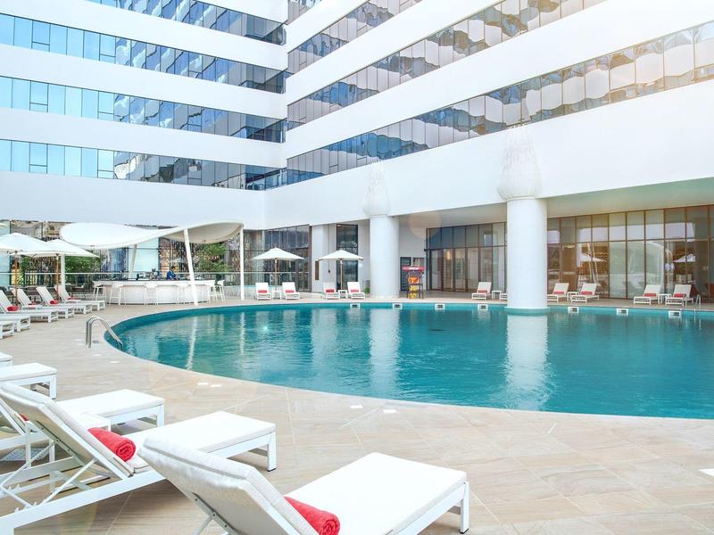 Modern hotel lobby pool with lounge chairs around and large glass windows in the background.