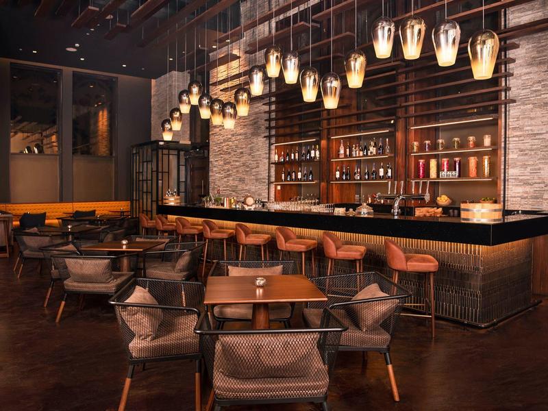 Cozy hotel bar with warm lighting, wooden chairs, and a long bar counter.