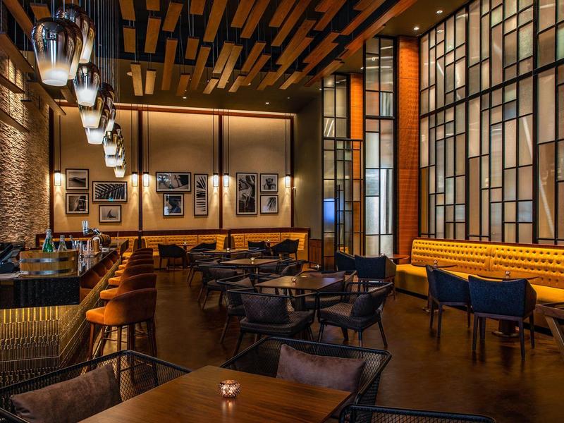 Modern hotel restaurant with dark interior, wooden ceiling, and cozy seating areas.