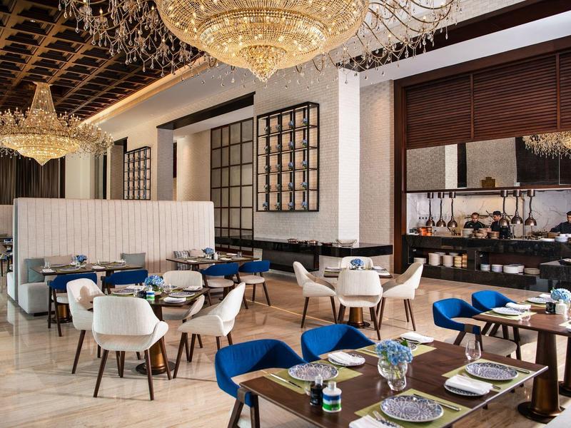 Elegant hotel restaurant with blue and white chairs, set tables, and chandeliers.