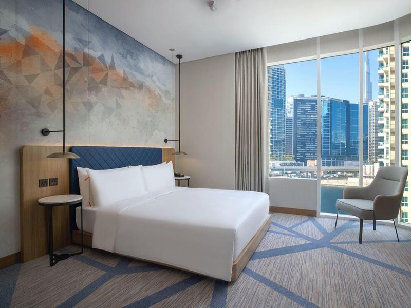 Helles Hotelzimmer mit großem Bett, moderner Wandgestaltung und Fenster mit Stadtblick.