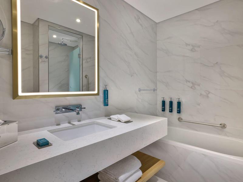 Modernes Badezimmer mit weißer Badewanne, beleuchtetem rechteckigem Spiegel und grauen Marmorwänden.