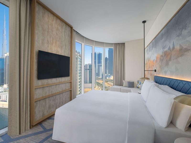 Modernes Hotelzimmer mit großem Bett, Panoramafenstern und Stadtblick bei Tageslicht.