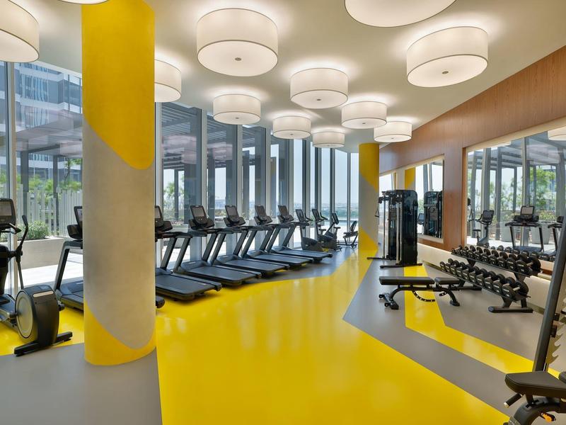 Modernes Fitnessstudio mit gelbem Boden, vielen Laufbändern und Hanteln an der rechten Seite.